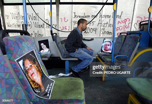 An Israeli Jew sits next to pictures of Israelis killed during different suicide attacks, inside the remains of a bus destroyed by a Palestinian...