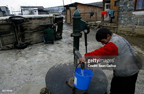 Young Roma man draws drinking water from the local well while another repairs a car February 26, 2004 in the Roma, or gypsy, slum of Bystrany in...