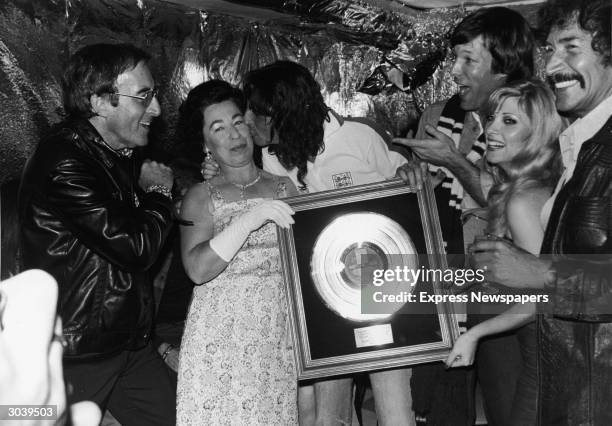American rock singer Alice Cooper kisses Queen Elizabeth II impersonator Jeanette Charles while holding his gold record plaque as L-R: actors Peter...