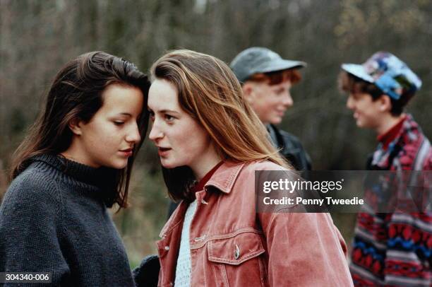 teenagers outdoors, two girls whispering in foreground - whispering stock pictures, royalty-free photos & images