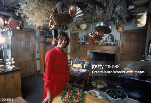 American media mogul and businesswoman Martha Stewart stands in a kitchen in a red dress, August 1976. Behind her is a table set with plates, wine,...