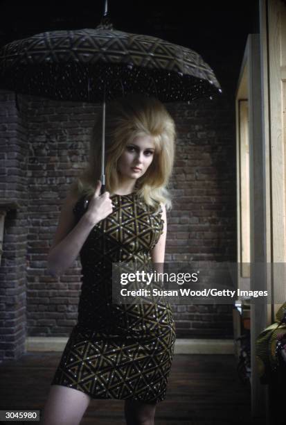 Actress Pamela Tiffin poses in a green and black dress with a triangular pattern and holds a matching umbrella, April 1966.