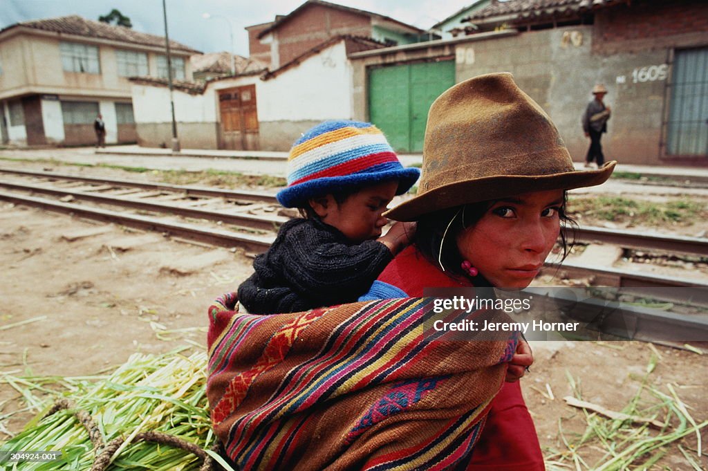 Peru,Cuzco,Quechua Indian girl with sibling on back,selling leeks