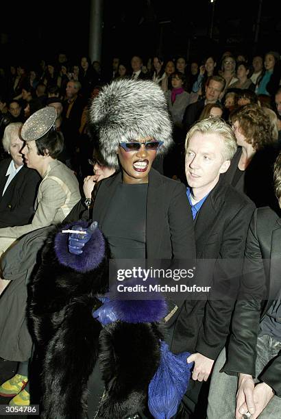 Model Grace Jones sits on designer Philip Treacy's knee during the Alexander McQueen ready-to-wear Fall-Winter collection 2004-2005 fashion show on...