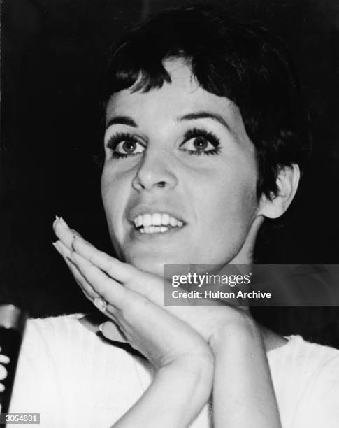 Headshot of French singer and actor Claudine Longet clasping her hands at a microphone during a visit to Japan, circa 1968.