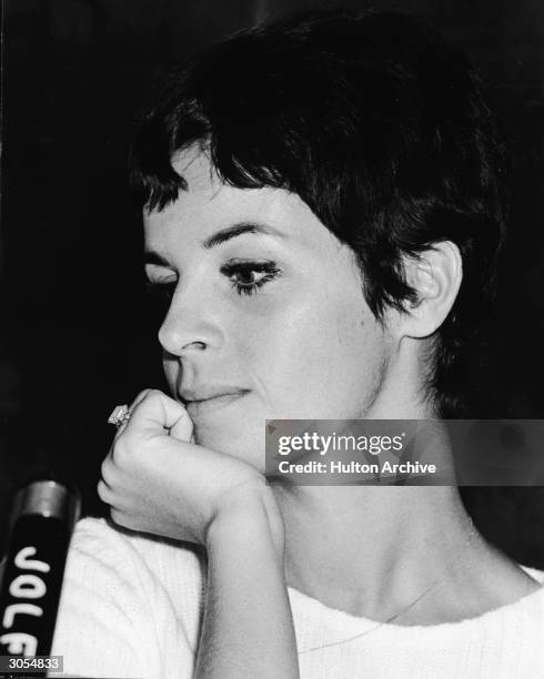 Headshot of French singer and actor Claudine Longet sitting at a microphone with her chin propped in her hand during a visit to Japan, circa 1968.