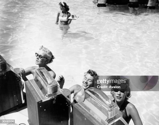 Three women play the slot machines at a swimming pool casino in the Sands Hotel, Las Vegas, Nevada. A wading waitress with a tray makes her way...