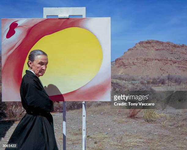 American artist Georgia O'Keeffe poses outdoors beside an easel with a canvas from her series, 'Pelvis Series Red With Yellow,' Albuquerque, New...