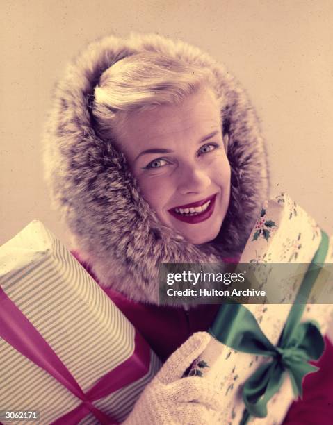 Model wearing a coat with a fur lined hood and carrying christmas presents.