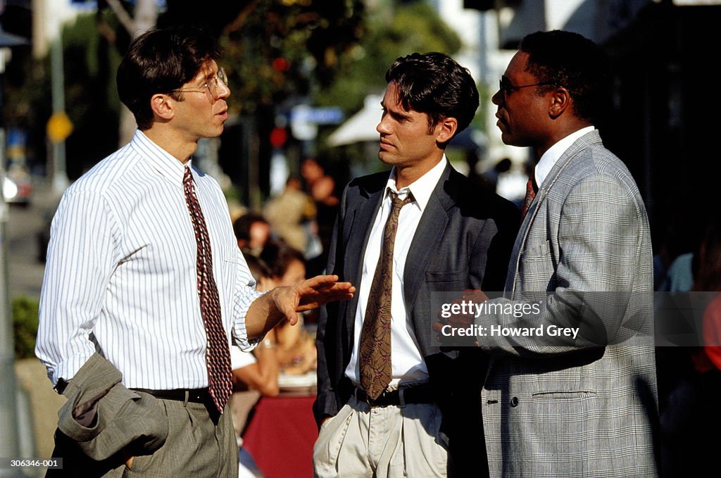 Portrait of three male executives in discussion on busy street
