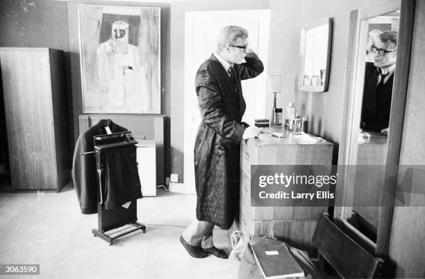 Clad in a dressing gown while his suit hangs on the trouserpress, British actor Michael Caine examines his reflection in the mirror.