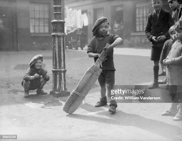 Group of children in a slum area of London's King's Cross play an improvised game of cricket with a lamppost as a wicket and a bat tied together with...