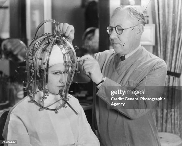 Hollywood cosmetics expert Max Factor takes precise measurements of a young woman's head and face with a contraption like an instrument of torture.
