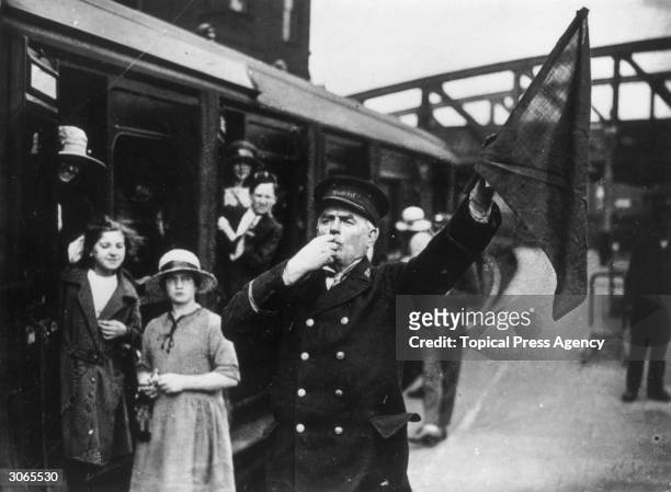 Richard James, a Great Western Railway guard waves his flag and blows his whistle to send a train on its way.