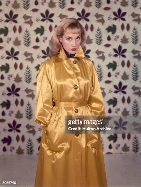 English actress Sylvia Syms wearing a gold raincoat.