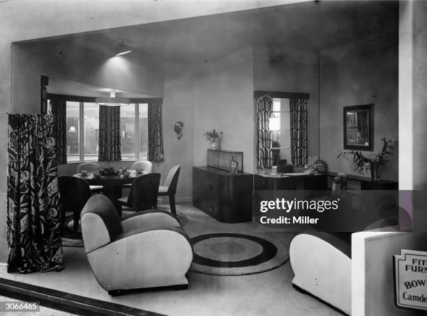 Bowman Brothers stand showing a living room at the ideal Home Exhibition, Olympia, London. On show are easy chairs with rounded edges, a round dining...