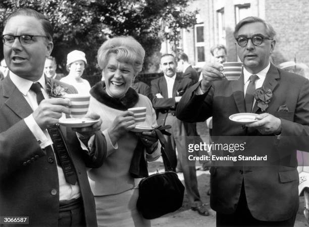 On the right, wearing a campaign rosette, deputy-leader of the Labour party, George Brown enjoying a cup of tea at a garden party.