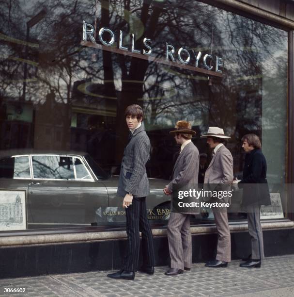 British pop group The Bee Gees, formerly The Brothers Gibb gaze through the window of a Rolls Royce showroom.