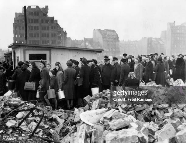 Citizens of Hamburg queuing among the ruins for their soup rations. They have pails and buckets as each recipient is allowed rations for five people.