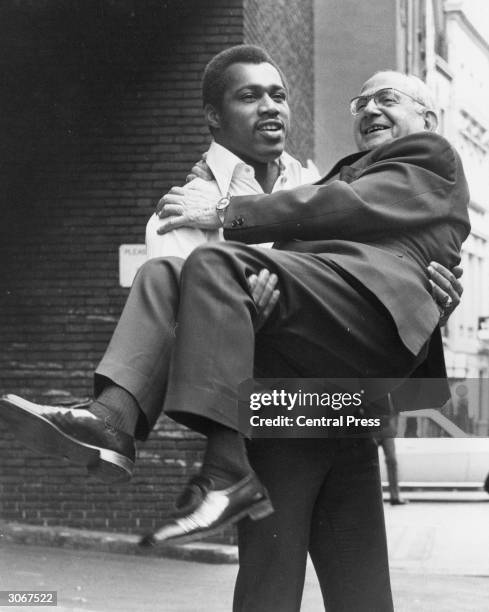 American heavyweight boxer Ken Norton gives a lift to boxing promoter Jack Solomons outside the Hertford Club, where he is attending a reception...