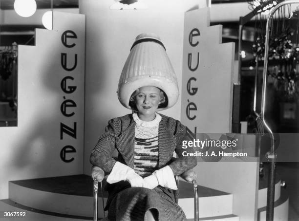 Woman having her hair dried under a large helmet-like dryer at a Hairdressing Fair, Olympia, London. She is wearing gauntlets.
