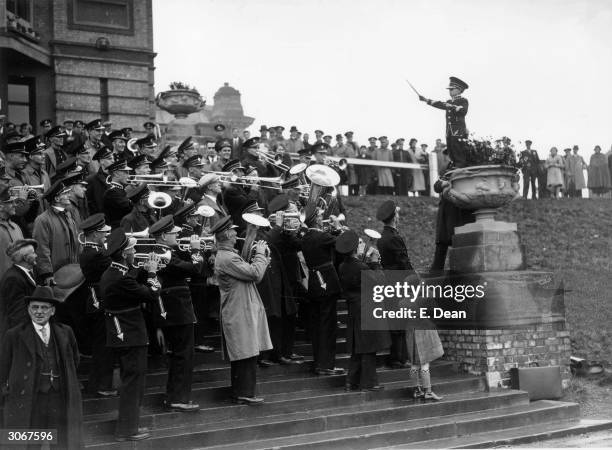 Wearing military uniform and peaked cap a small boy stands on a large stone urn as he conducts during Brass Band Day at Alexandra Palace, north...