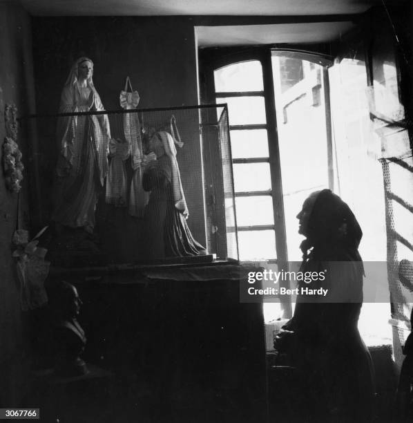 An old woman praying before an icon depicting St Bernadette and the Virgin Mary, at the saint's house in Lourdes.