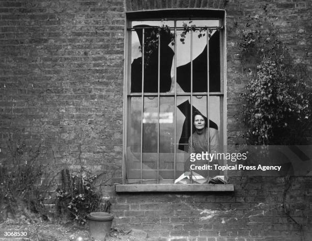 Woman peers through a shattered window the day after a bomb attack by suffragettes on nearby Holloway prison, 19th December 1913. Two bombs, were...