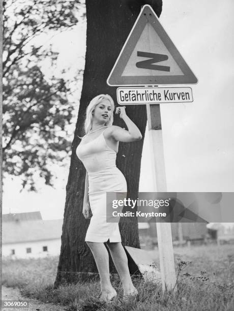 Curvaceous German actress Barbara Valentin poses beside a road sign which reads 'Dangerous Curves' in German.
