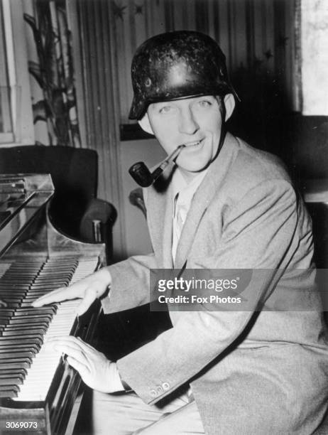 American entertainer Bing Crosby playing the piano and wearing a German helmet.