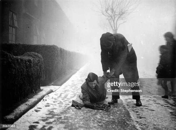 Man stoops to help an unwary pedestrian who has slipped on an icy pavement in Walthamstow, East London.