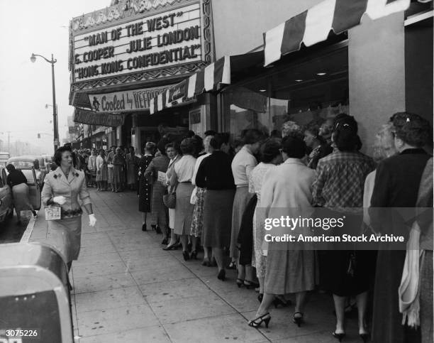 Women line up outside a theater showing Gary Cooper and Julie London in 'Man of the West,' 1958. Also advertised on the marquee is 'Hong Kong...