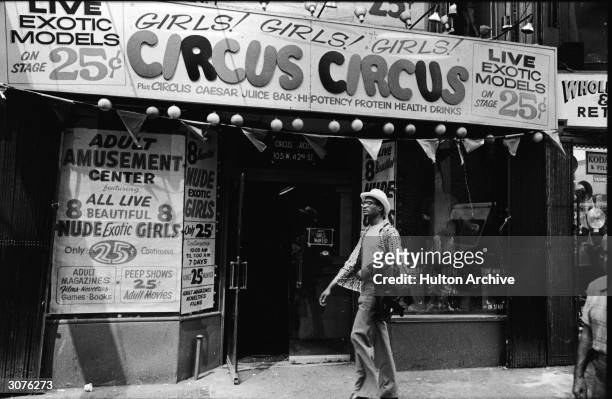 Exterior view of Circus Circus, an 'adult amusement center,' in Times Square as a man walks past wearing a hat and carrying his coat over his arm,...