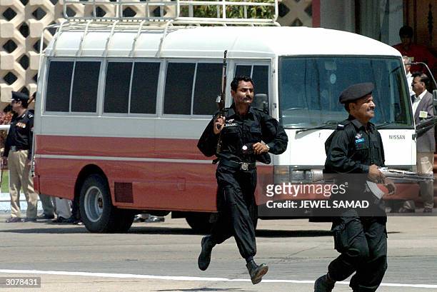 Two Pakistani police commandos run before a bus transporting the Indian cricket team upon their arrival at Jinnah International Airport in Karachi,...