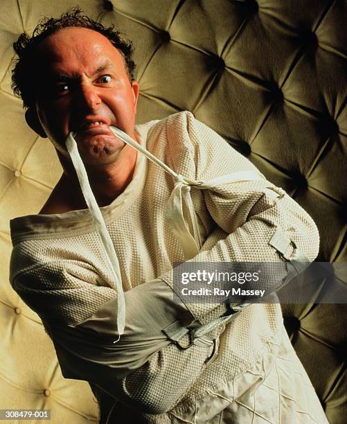 man in padded cell wearing strait- jacket, pulling strap with teeth - dwangbuis stockfoto's en -beelden