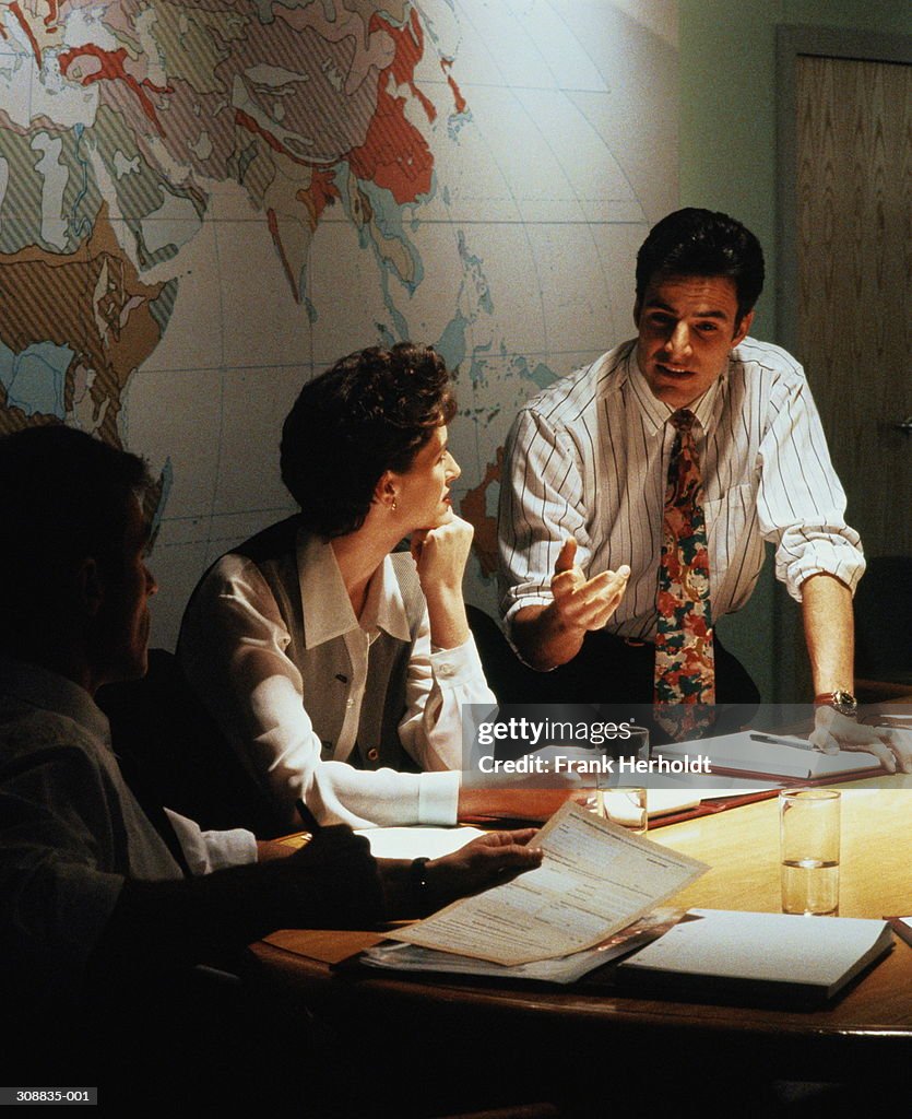 Woman and two men in discussion around table,world map behind