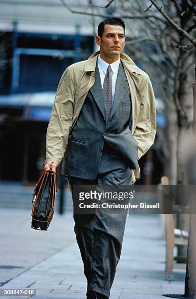 male executive with briefcase walking down street,outdoors - trench coat stock pictures, royalty-free photos & images