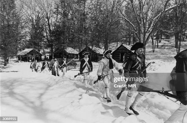 Band of men dressed as colonial soldiers march past a row of reconstructed log cabins in Valley Forge National Historical Park, Pennsylvania. The...