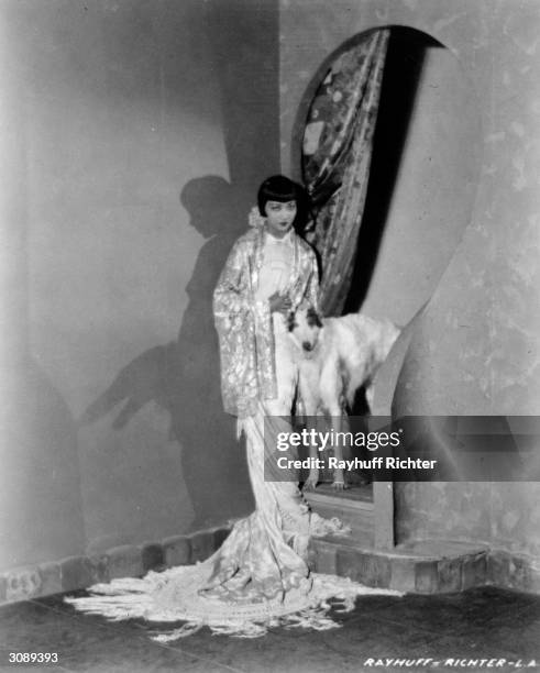 Chinese-American actress Anna May Wong wearing a flowing gown and standing next to a lean hound.