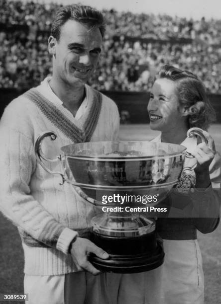 Captain of the US Davis Cup team, Vic Seixas holds the trophy for winning the men's singles championship of Victoria assisted by Maureen Connolly who...