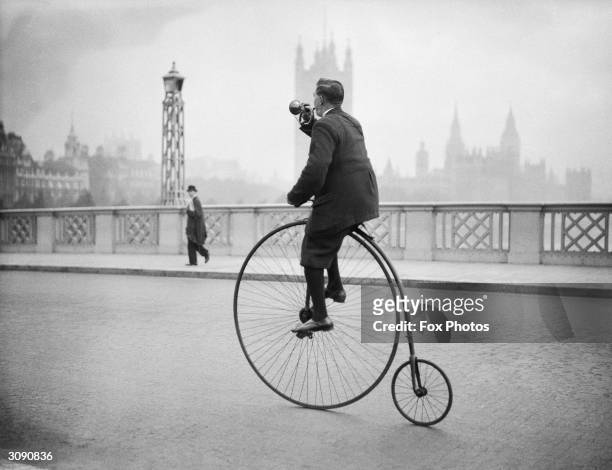 Edwin Davey, riding a penny farthing bicycle over Lambeth bridge in London, and blowing a bugle to warn of his approach.