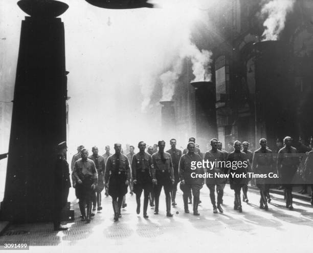 Adolf Hitler and Hermann Goering march in Munich to commemorate the 1923 putsch. They pass the 16 red-draped pylons topped with flaming bowls, each...