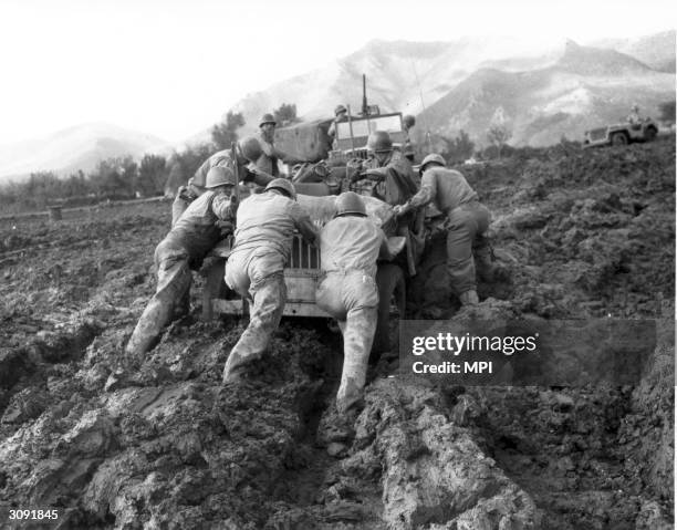 Allied soldiers struggle to push a jeep through mud during WW II in Italy.