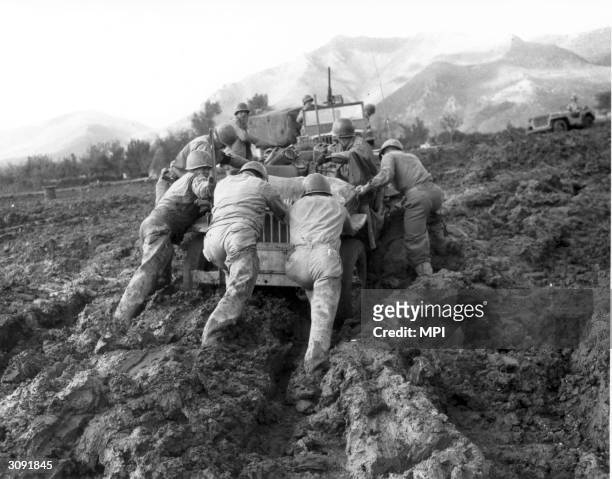 Allied soldiers struggle to push a jeep through mud during WW II in Italy.