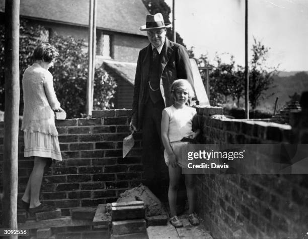 British Chancellor of the Exchequer Winston Leonard Spencer Churchill enlists the help of his two daughters Sarah and Mary in building the brick wall...