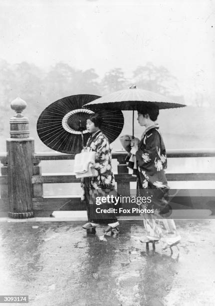 Under umbrellas two Japanese women cross Benkei Bashi bridge in Tokyo.On their feet they wear geta, wooden sandals with supports, special geta with...