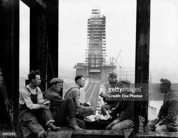 Construction workers take a lunch break with the 300 ft high chimney of Battersea Power station, which is nearing completion, in the background,...
