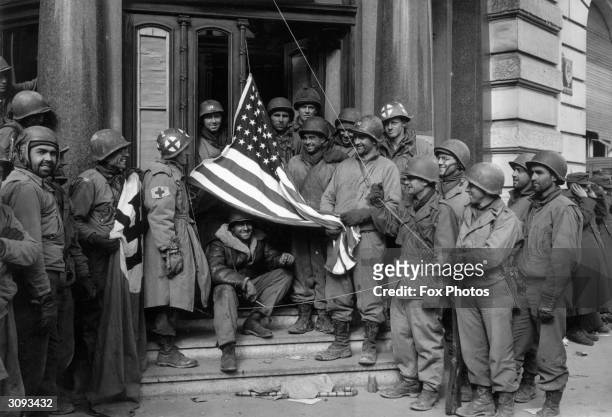 Soldiers of the US Third Army exchange the Nazi swastika in front of the Porta Negre Hotel - the Nazi headquarters in Trier - for an American flag...