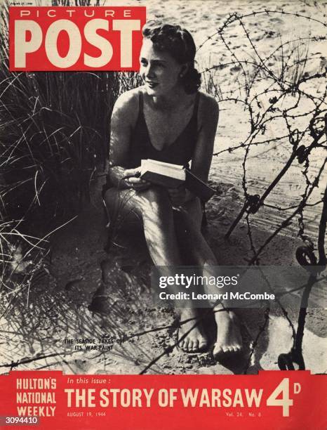 Young woman relaxes on a British beach with a book, but a tangle of barbed wire reminds her that the war is still raging in Europe. The headline...