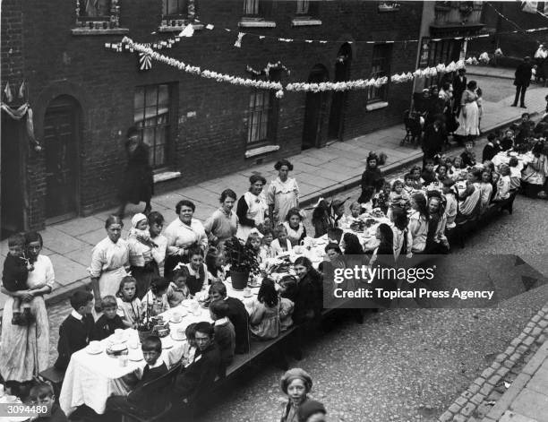 London street party on Peace Day July 1919. A long trestle table has been set up with food and paper chains decorate the street.